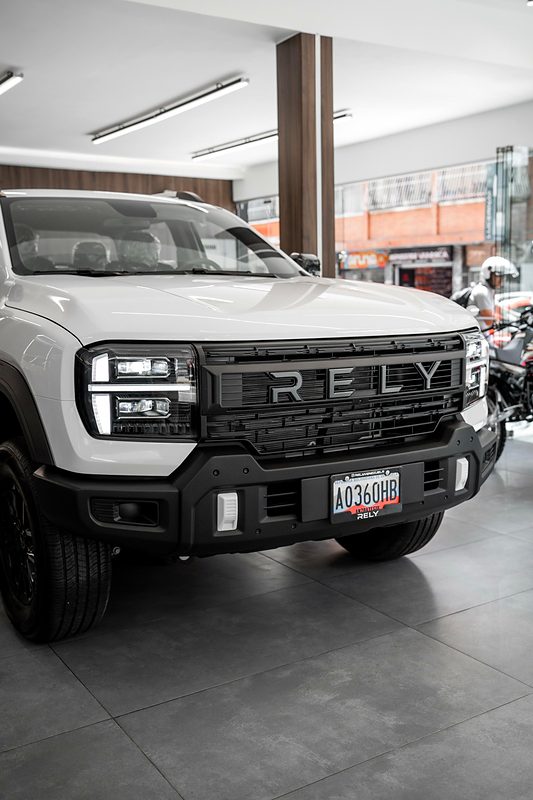 Frontal de la RELY R8 blanca con faros LED y parrilla RELY en el showroom de Caracas