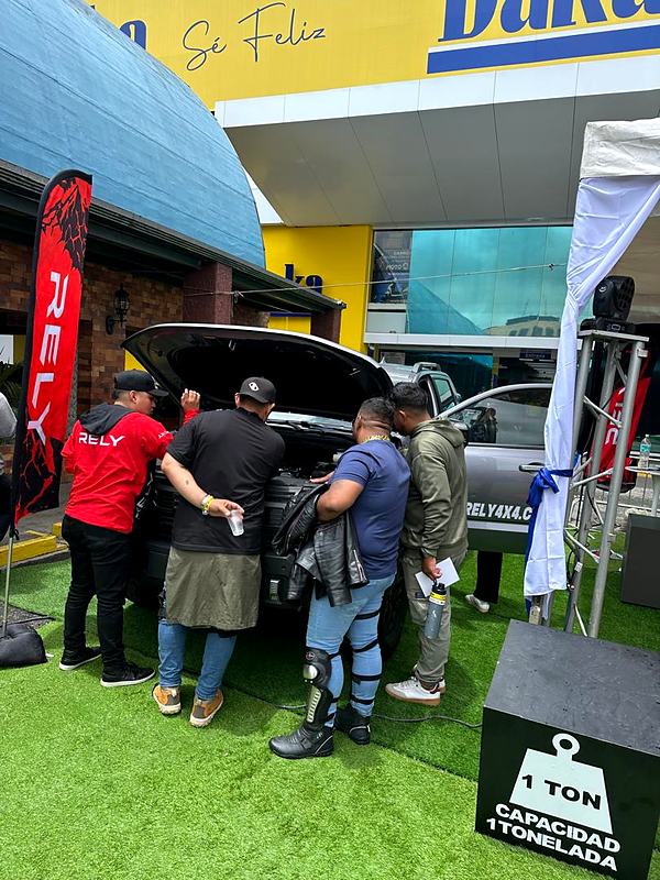 Visitantes miran el motor de una RELY R8 frente a Daka, junto al cartel de capacidad de 1 tonelada