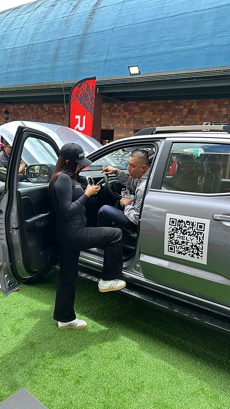 Visitantes revisan una RELY R8 gris con código QR durante el evento de RELY frente a una tienda Daka