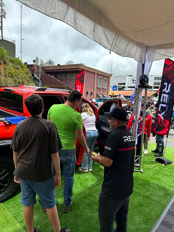 Visitantes conocen la RELY R8 roja bajo la carpa de RELY en un evento al aire libre